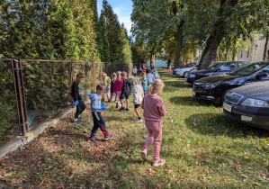 Ludzie wyrzucają śmieci z samochodów na trawę a kosz jest po drugiej stronie ulicy.